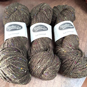 以下が含まれることがあります： 色の斑点のある茶色の糸の3つの巻き。糸は「スタジオ・ドネガル ソフト・ドネガル」とラベル付けされています。