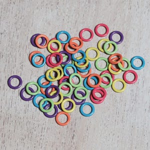 May include: A pile of colorful plastic rings, in shades of green, yellow, orange, red, purple, and blue. The rings are arranged in a random pattern on a light wood surface.