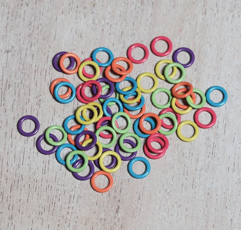 May include: A pile of colorful plastic rings, in shades of green, yellow, orange, red, purple, and blue. The rings are arranged in a random pattern on a light wood surface.