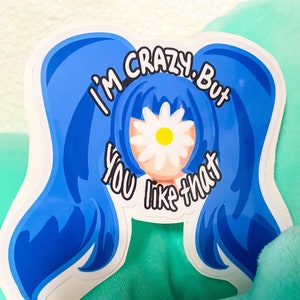 Puede incluir: Una pegatina blanca con un personaje de dibujos animados azul con coletas azules y una margarita que cubre la cara. El texto en la pegatina dice "Estoy loco, pero te gusta eso."