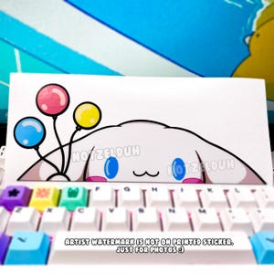May include: A white sticker with a cartoon character design, blue eyes, pink mouth, and three balloons. The sticker is on a white keyboard with colourful keycaps. The text on the sticker reads "NOTZELDUH" and "ARTIST WATERMARK IS NOT ON PRINTED STICKER. JUST FOR PHOTOS :)".
