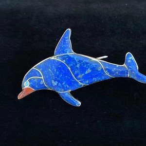 May include: A silver and lapis lazuli dolphin brooch. The dolphin is blue with silver accents and a red mouth.