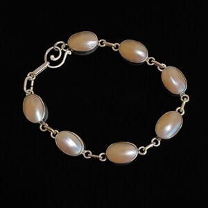 Peut inclure: Un bracelet en argent avec des pierres ovales en nacre. Le bracelet a une chaîne délicate et un fermoir.