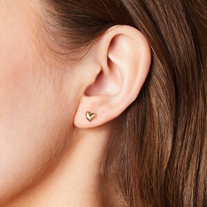 May include: A pair of gold heart-shaped stud earrings. The earrings are small and delicate, and they are perfect for everyday wear.