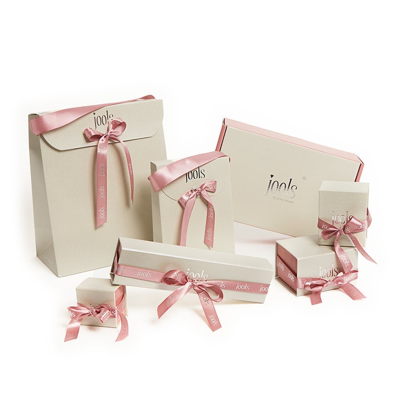 May include: A set of six gift boxes in various sizes, all featuring a cream-colored background with the word "jools" printed in a silver font. The boxes are tied with pink satin ribbon and bows.