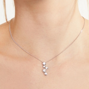 Peut inclure: Un collier en argent délicat avec un pendentif en grappe de cinq pierres précieuses rondes et transparentes. Le pendentif est suspendu à une fine chaîne, créant un design minimaliste et élégant. Les pierres sont serties dans un sertissage argenté.