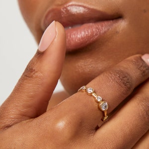 Könnte beinhalten: Ein goldener Ring mit einer Reihe kleiner, klarer runder Steine.