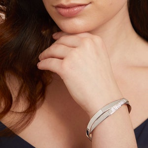 May include: Silver bangle bracelet with a textured design. The bracelet is made of two bands that are intertwined.
