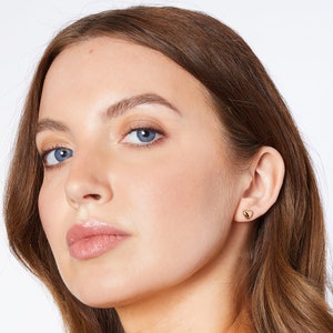 May include: A close-up of a person's face with a small gold heart-shaped earring in their right ear.