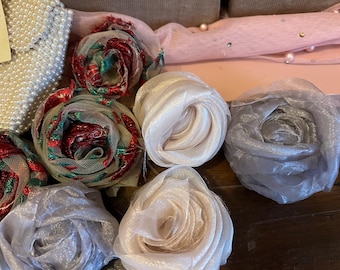 May include: An assortment of fabric flowers in various colors, including red, white, and gray. Some flowers are made of sheer, layered material, while others have a mesh overlay. A beaded item is visible in the background.