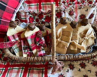 May include: A wicker basket filled with handmade Christmas ornaments. Each ornament is a brown paper tag tied with a red and green plaid ribbon and a small brown jingle bell.