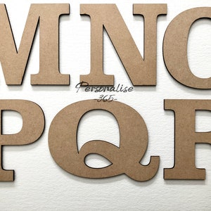May include: Six individual capital letters made of light brown wood, arranged in two rows. The top row displays the letters M, N, and O, while the bottom row shows P, Q, and R. The text Personalise-365- is printed in black between the two rows.