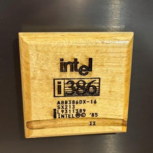 May include: A light-coloured wooden Intel i386 processor with black text. The text includes the Intel logo, "i386", and other model information. The processor is rectangular with a dark background.