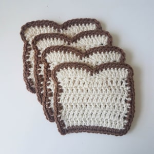 May include: Four crocheted coasters shaped like slices of bread. The coasters are white with brown edges.