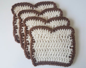 May include: Four crocheted coasters shaped like slices of bread. The coasters are white with brown edges.