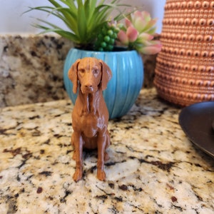 May include: A brown 3D printed figurine of a dog sitting on a granite countertop. The dog has a short, smooth coat and is looking directly at the camera.