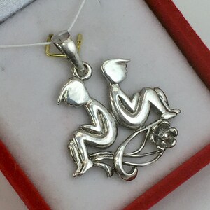 May include: Silver pendant featuring a stylized depiction of the Gemini zodiac sign, two figures intertwined with a floral design.