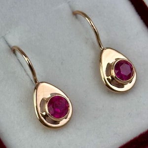 Peut inclure: Une paire de boucles d'oreilles en or avec un design en forme de larme. Chaque boucle d'oreille présente une seule pierre rouge ronde.
