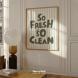 May include: A framed wall art print with the words "So FRESH and SO CLEAN" in a playful, dark green font. The background has vertical stripes in light green and white. The frame is a warm gold color.