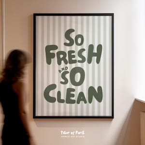 May include: A framed art print with the words "So Fresh and So Clean" in a bold, green font. The background features vertical stripes in light green and white. The print is in a black frame.
