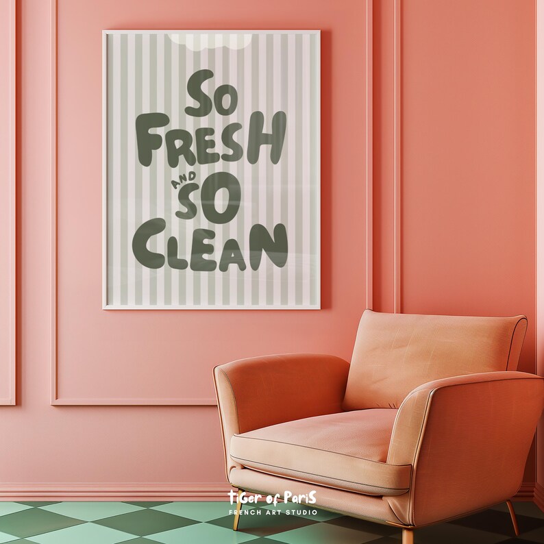 May include: A framed print with the words "So Fresh and So Clean" in a playful font. The background has vertical stripes in shades of gray. The print hangs on a pink wall above a peach-colored armchair.