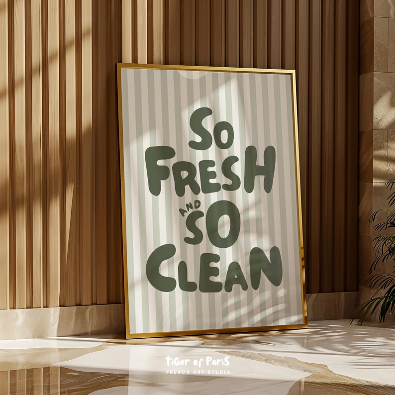 May include: A framed art print with a gold border. The print features the words "So Fresh and So Clean" in a green, playful font against a striped background of white and light green. The bottom of the print has the text "Tiger of Paris" and "French Art Studio".