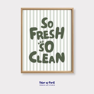 May include: A framed print with the words "So Fresh and So Clean" in dark green, bold letters. The background features vertical light green and white stripes. The frame is a light brown color. The text "tiger of Paris FRENCH ART STUDIO" is at the bottom.