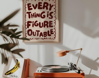 May include: A framed print with the words "EVERY THING IS FIGURE OUTABLE" in maroon lettering. Below, an orange record player with a record and a banana album cover. A small orange lamp is positioned above the record player.