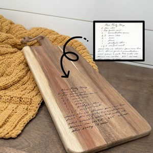 May include: A wooden cutting board with a handwritten recipe for "Ches Party Mix" engraved on the surface. The recipe includes ingredients like pretzels, cheese, and nuts. The board is brown with a natural wood grain.