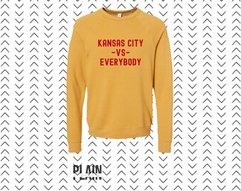 May include: A mustard yellow sweatshirt with the text "KANSAS CITY -VS- EVERYBODY" in red.