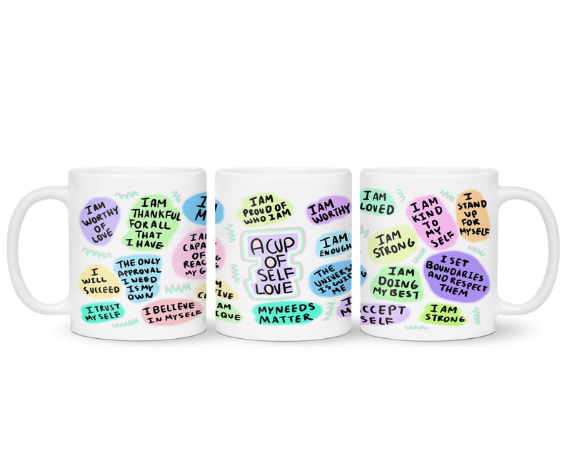 May include: Three white ceramic mugs with colorful text and illustrations. The text on the mugs includes phrases like "I am worthy of love", "I am thankful for all that I have", "A cup of self love", "I am loved", "I am strong", "I am kind to myself", "I stand up for myself", "I set boundaries and respect them", and "I am strong".