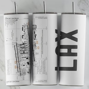 May include: Three white insulated tumblers with silver straws. The tumblers feature a detailed airport diagram, the text "LOS ANGELES INTL (LAX)", and the letters "LAX" in black. The design is printed on the white surface.