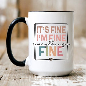 May include: White ceramic mug with a black handle. The mug has a graphic design that says "It's fine I'm fine everything's fine" in colorful text with a small heart at the bottom.