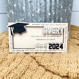 May include: A wooden graduation sign with a black graduation cap, the name Avery, and the text "class of 2024". The sign has a white background and black lettering.