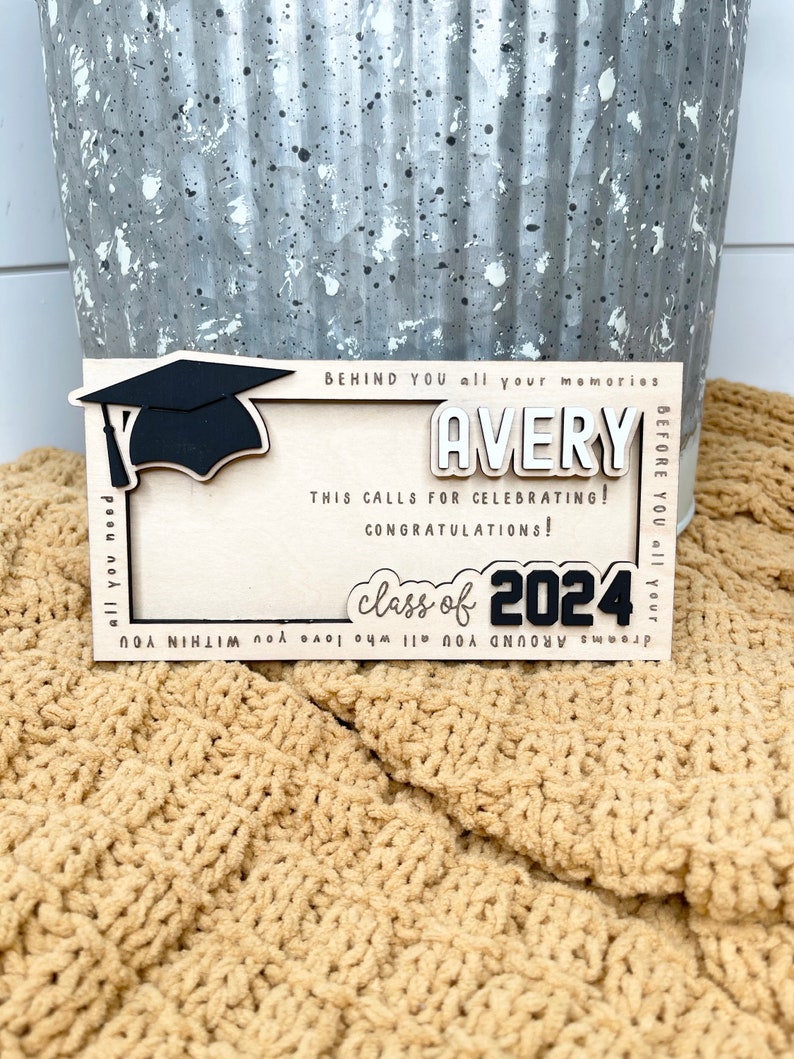 May include: A wooden graduation sign with a black graduation cap, the name Avery, and the text "class of 2024". The sign has a white background and black lettering.