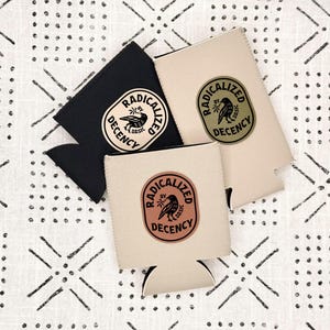 May include: Three foam beverage insulators in black, beige, and light tan. Each features a circular logo with a bird illustration and the text "RADICALIZED BY BASIC DECENCY". The black insulator has a cream logo, the beige one has a green logo, and the tan one has a brown logo.