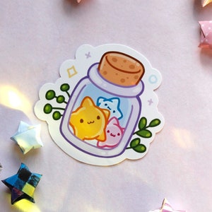 May include: A sticker of a glass jar with a cork stopper filled with three small, cartoon stars. The stars are yellow, blue, and pink. The jar is surrounded by green leaves.