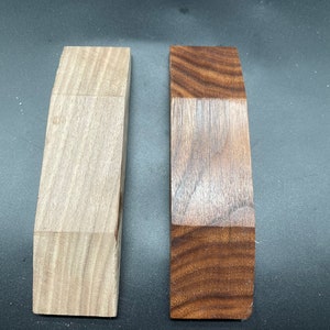 May include: Two wooden blocks, one light-colored and the other dark, with a curved top edge. The light block has a natural wood grain, while the dark block has a rich, contrasting grain. Both blocks are rectangular.