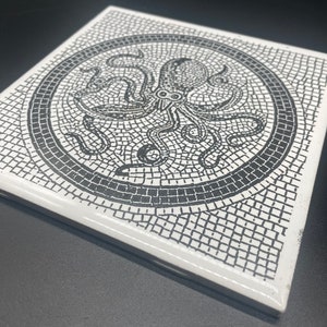 May include: Square white ceramic tile featuring a black mosaic design of an octopus. The octopus is centered within a circular border, surrounded by a mosaic pattern. The tile has a glossy finish and is suitable for home decor.