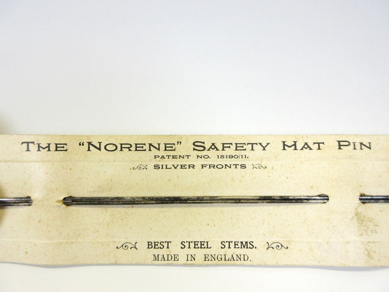 May include: Vintage "Norene" safety mat pins on a cream-colored card. The card reads "The 'Norene' Safety Mat Pin" with "Silver Fronts" and "Best Steel Stems. Made in England." The pins are silver.