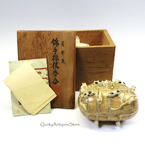 May include: An antique Japanese incense set featuring a decorative container with mice figures, a wooden box with Japanese text, and several paper inserts. The set is displayed on a white surface.