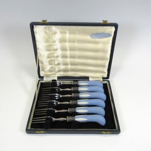 May include: A set of six silver forks with blue and white handles in a black velvet lined box. The box has a Wedgwood label.