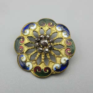 May include: A gold-toned metal button with a decorative design of swirls and a center cluster of rhinestones. The button is enameled in shades of blue, green, red, and white.