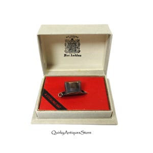 May include: A silver top hat charm in a white box with red lining. The box has the text "Mac Lachlan" and "925 Sterling Hat" printed on it.