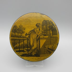 May include: A round, yellow tin lid with a black and white image of a woman in a garden setting. The woman is looking at a birdcage. The text "Wilson's Choice" is printed on the bottom of the lid.