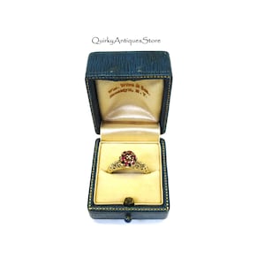 May include: A gold ring with a red gemstone center and smaller gemstones around the center. The ring is in a blue velvet ring box with a white interior. The box has the text "Wm. Wise & Co. Broadway, N.Y." printed on the inside.