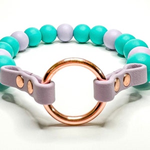 May include: A lavender leather dog collar with a rose gold ring and turquoise and lavender beads.