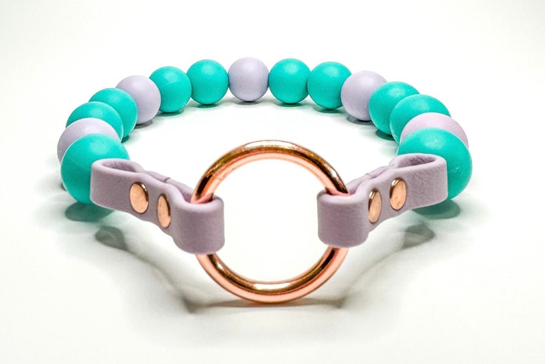 May include: A lavender leather dog collar with a rose gold ring and turquoise and lavender beads.