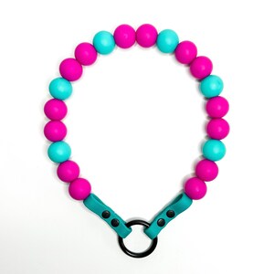 May include: A turquoise and pink beaded necklace with a black metal ring clasp. The necklace is made of silicone beads.