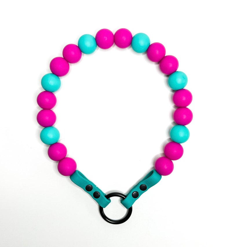 May include: A turquoise and pink beaded necklace with a black metal ring clasp. The necklace is made of silicone beads.